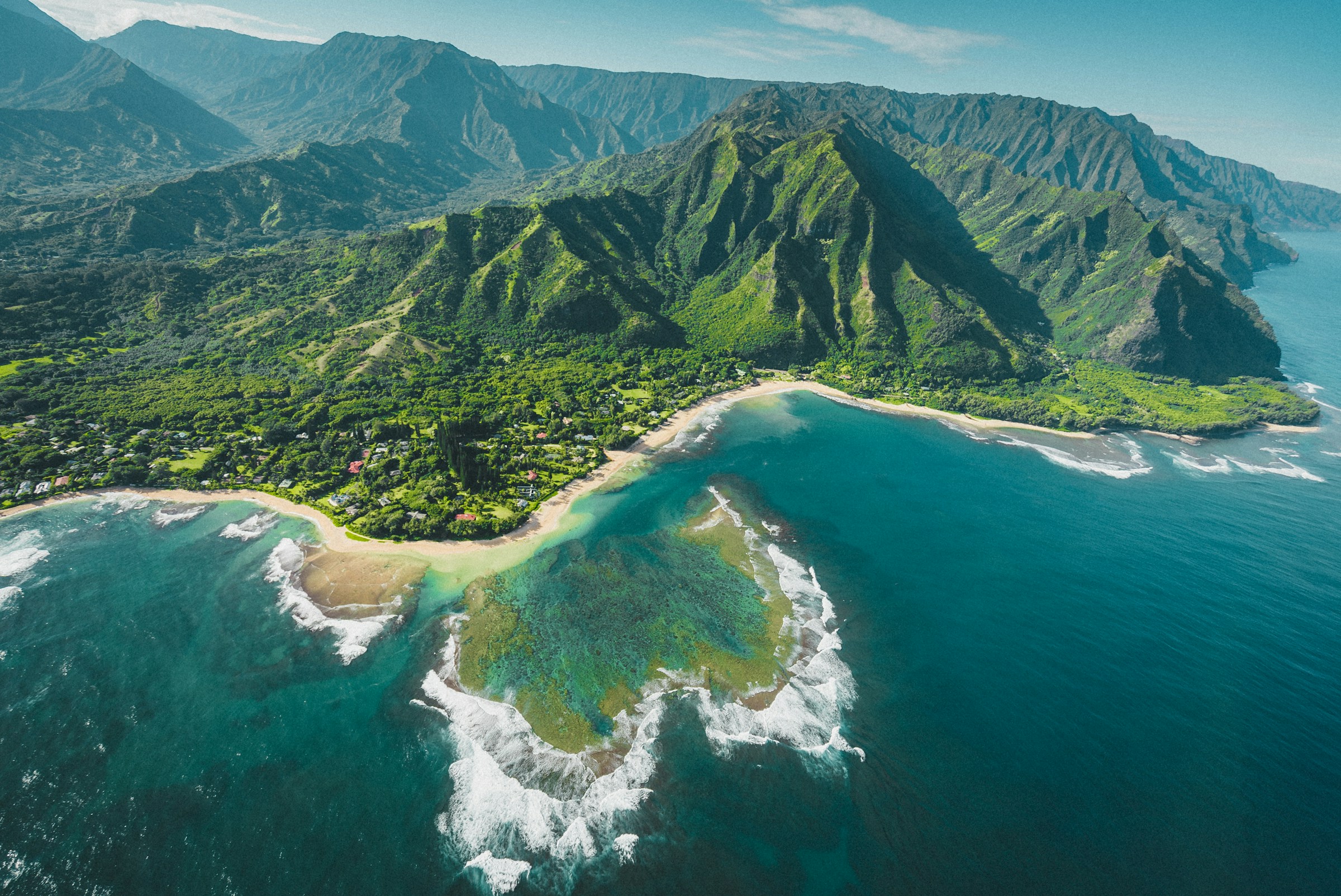 An aerial view of a lush green coastline, a turquoise reef and the open ocean on Kauai, Hawaii